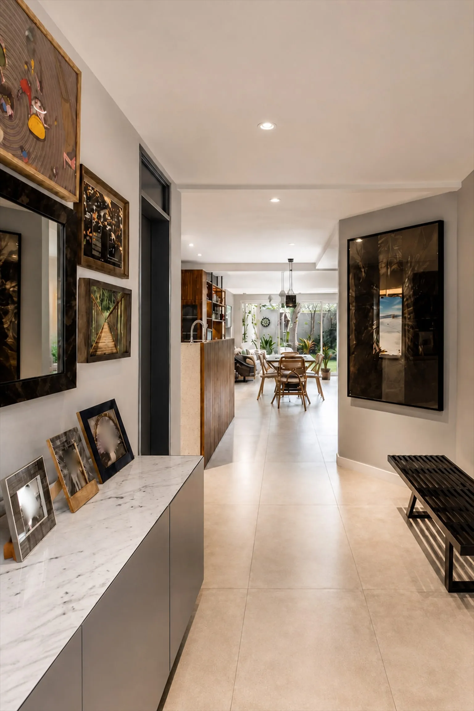 Hall de entrada com aparador de mármore e parede de quadros, corredor até a sala ao fundo