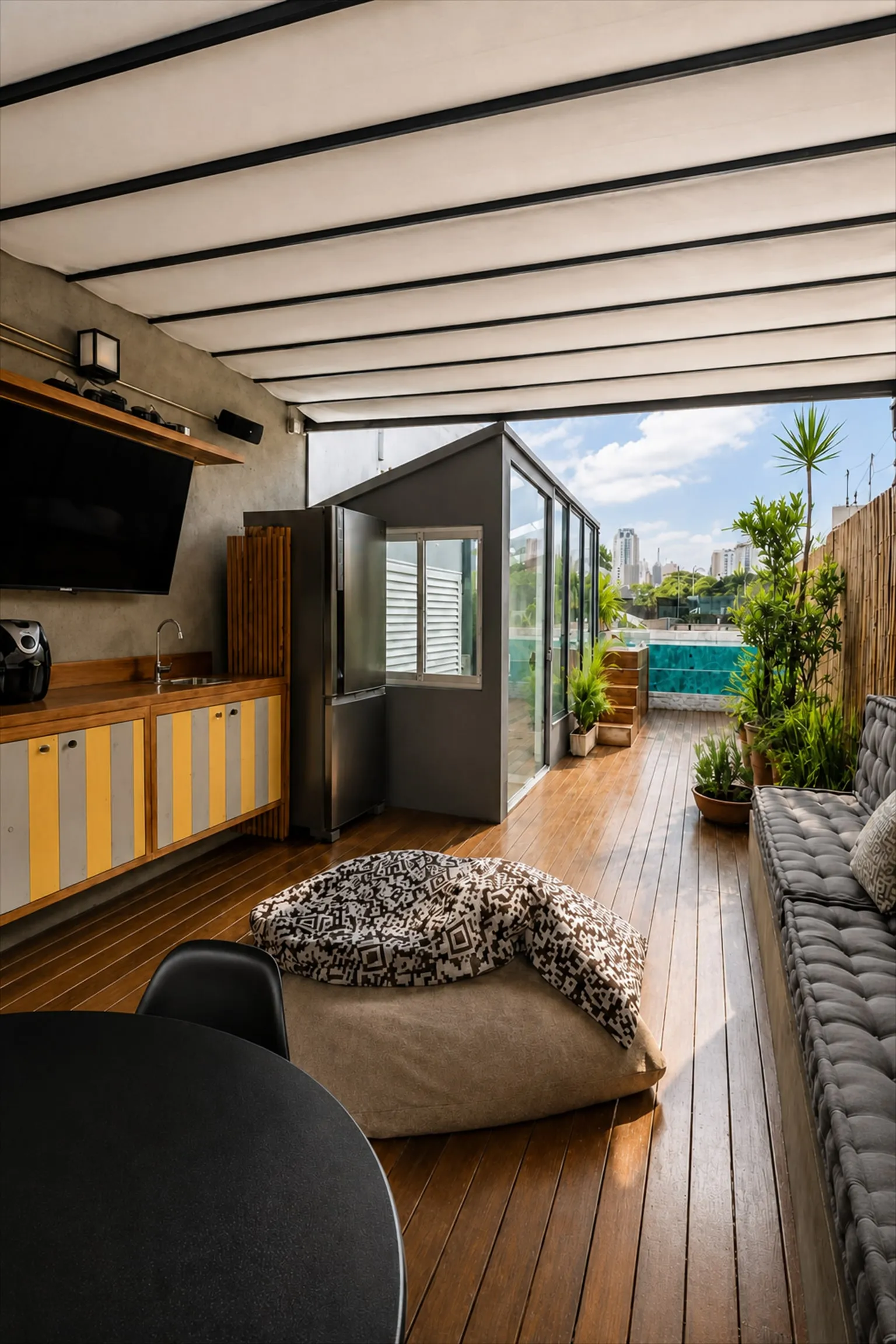 Cozinha externa do rooftop com bancada, armários, geladeira e TV, com vista para a piscina