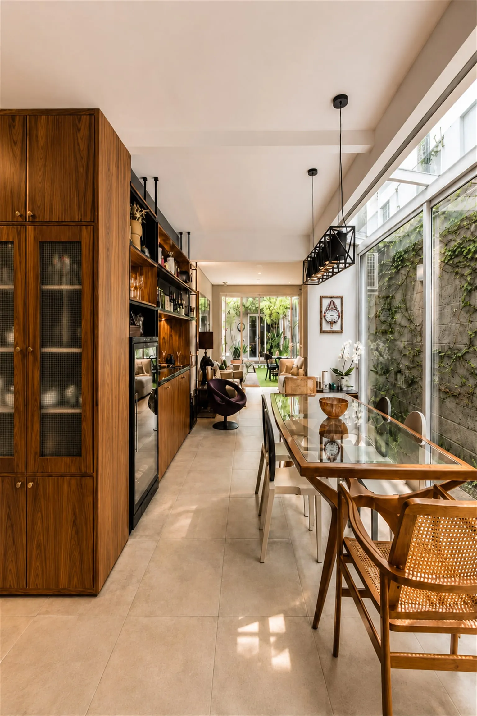 Sala de jantar com mesa de vidro, marcenaria escura com adega e jardim vertical na parede envidraçada